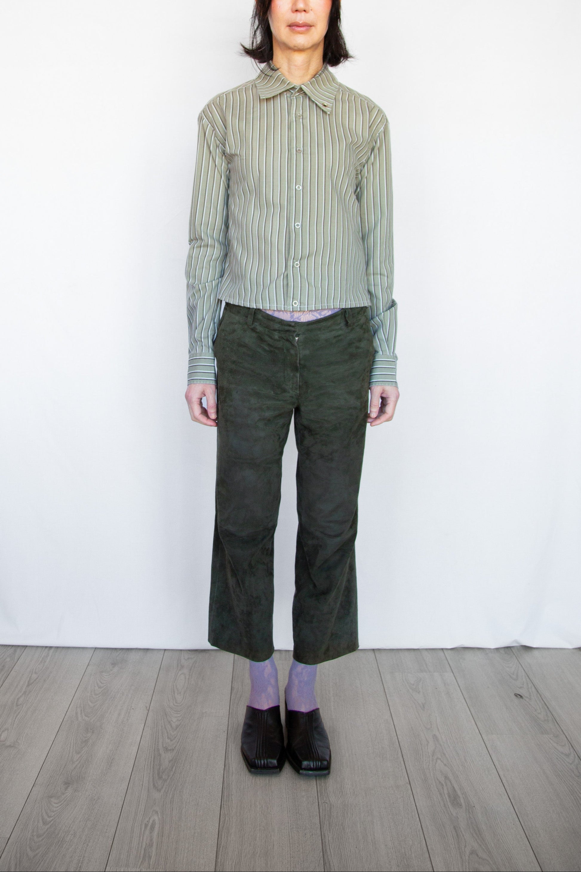 Person wearing a striped shirt and green pants against a white wall.